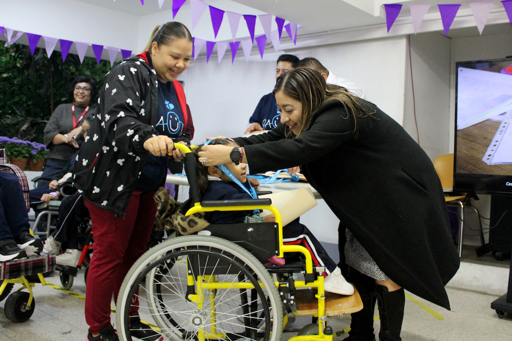 Guadalupe Maldonado, Directora General de APAC, entrega un reconocimiento a una beneficiaria en silla de ruedas por su proyecto premiado en la Feria Estatal PAUTA 2026, acompañada de su maestra.